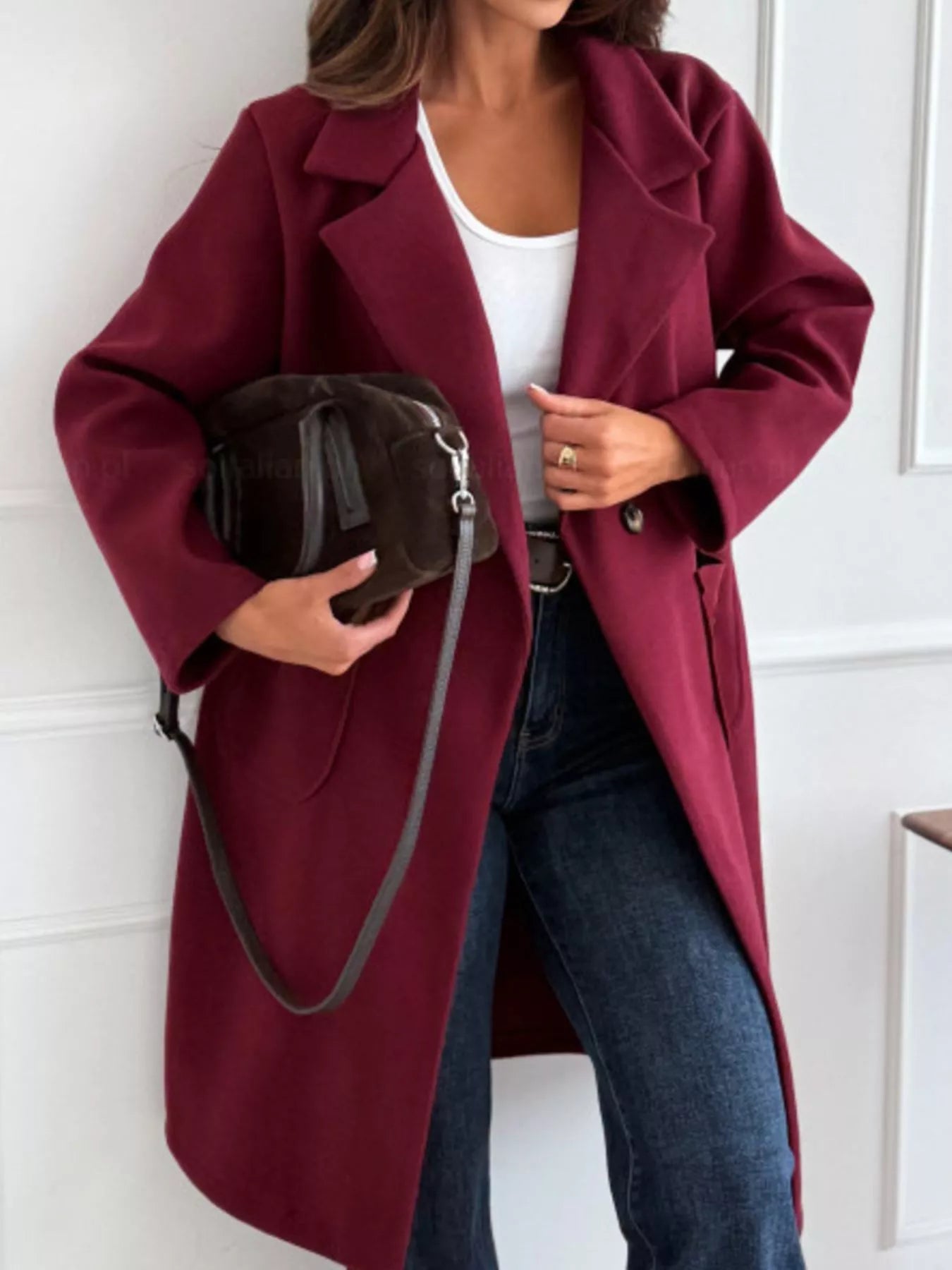 Person wearing a burgundy coat holding a black handbag against a white background