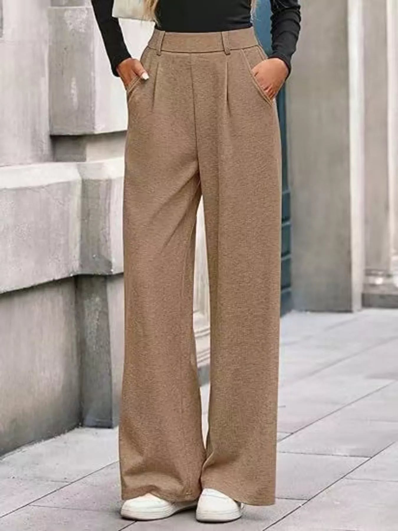 Person wearing beige wide-leg pants standing against a stone wall.