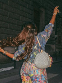Person with long hair wearing a colorful outfit and holding a gray handbag.