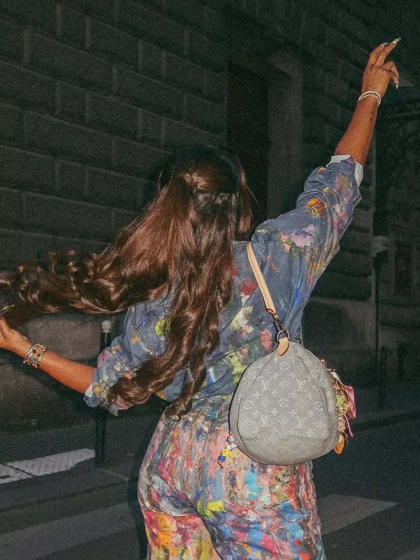 Person with long hair wearing a colorful outfit and holding a gray handbag.