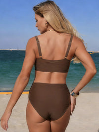 Woman in a brown bikini standing on a beach with ocean in the background