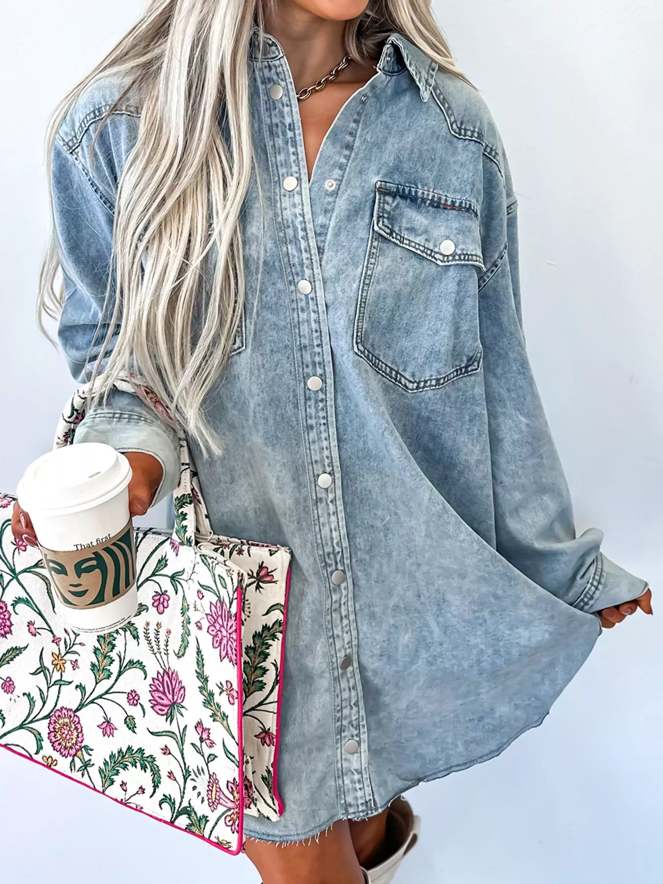 Person wearing a denim shirt with a floral bag and coffee cup on a white background