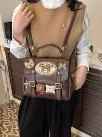 Person holding a brown handbag with bear-themed decorations indoors.