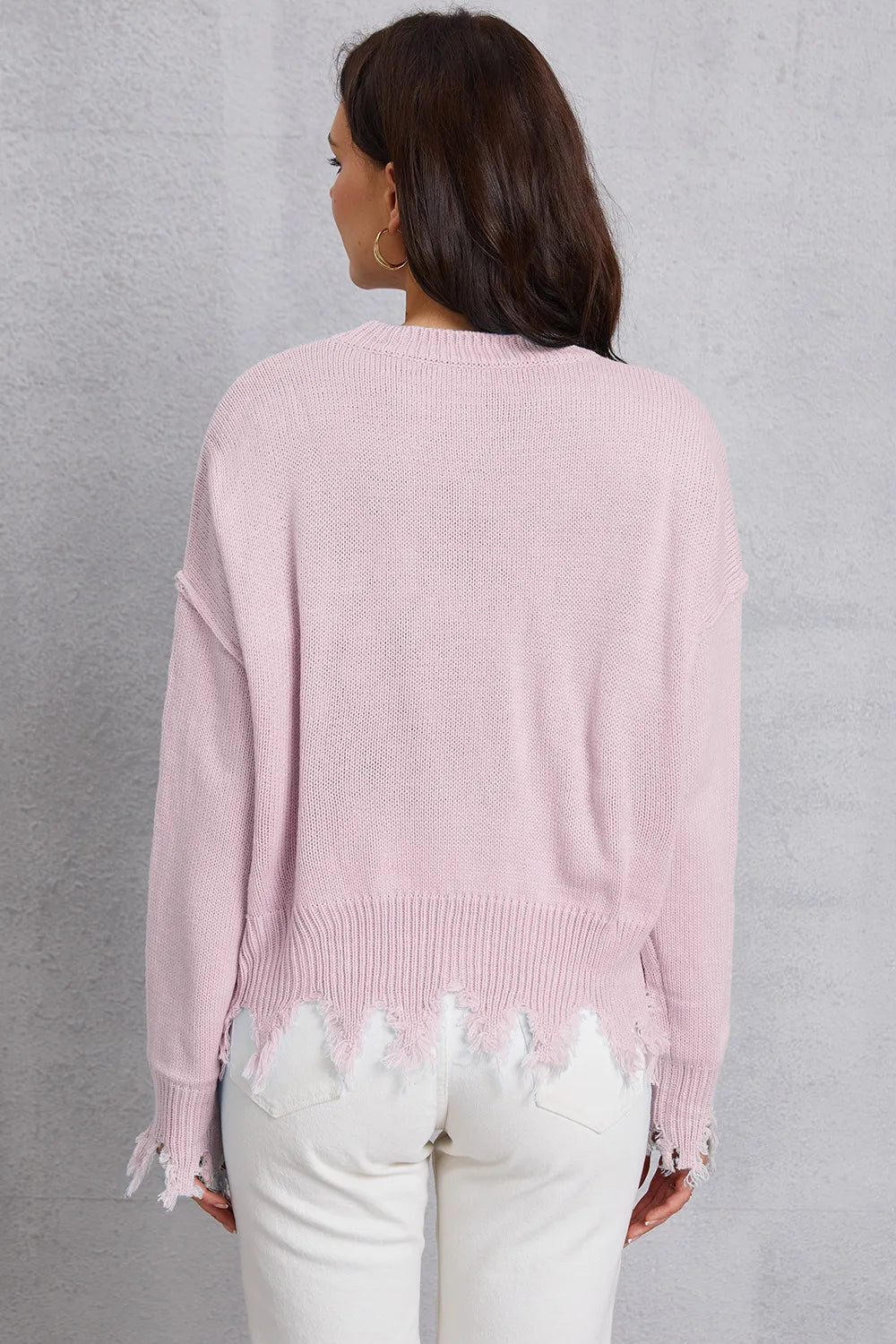 Person wearing a light pink sweater with fringe details on a gray background