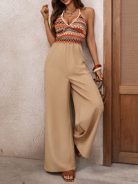 Woman wearing a patterned top and beige wide-leg pants against a textured wall.