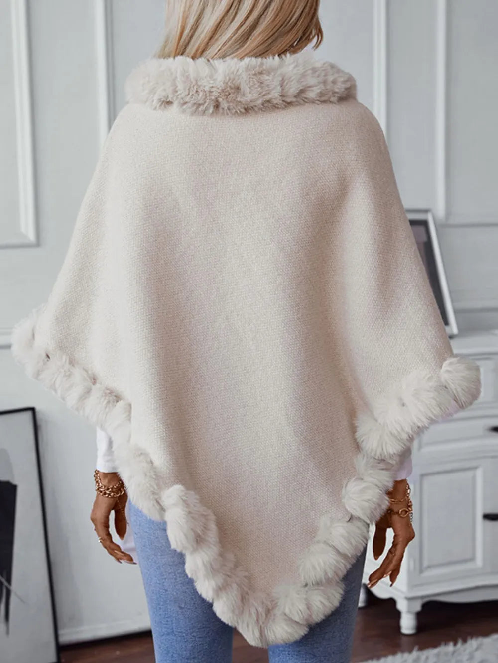 Person wearing a beige poncho with fur trim in a room setting.