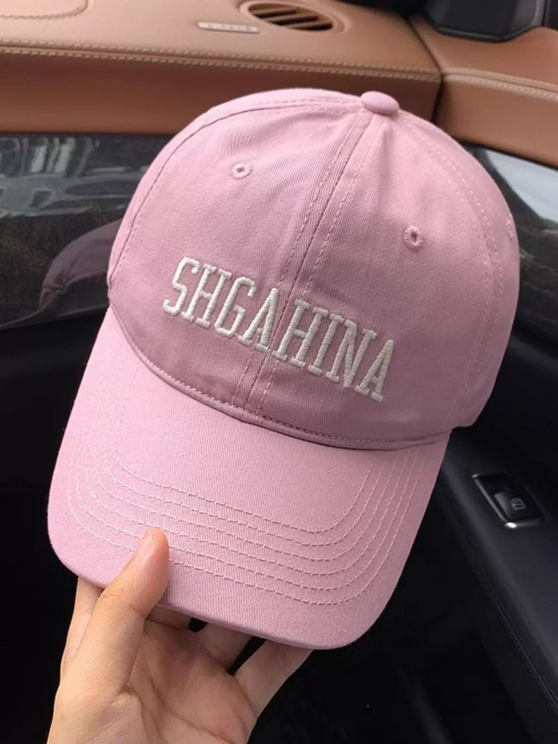 Pink cap with 'SHGAHINA' text held in front of a car interior.