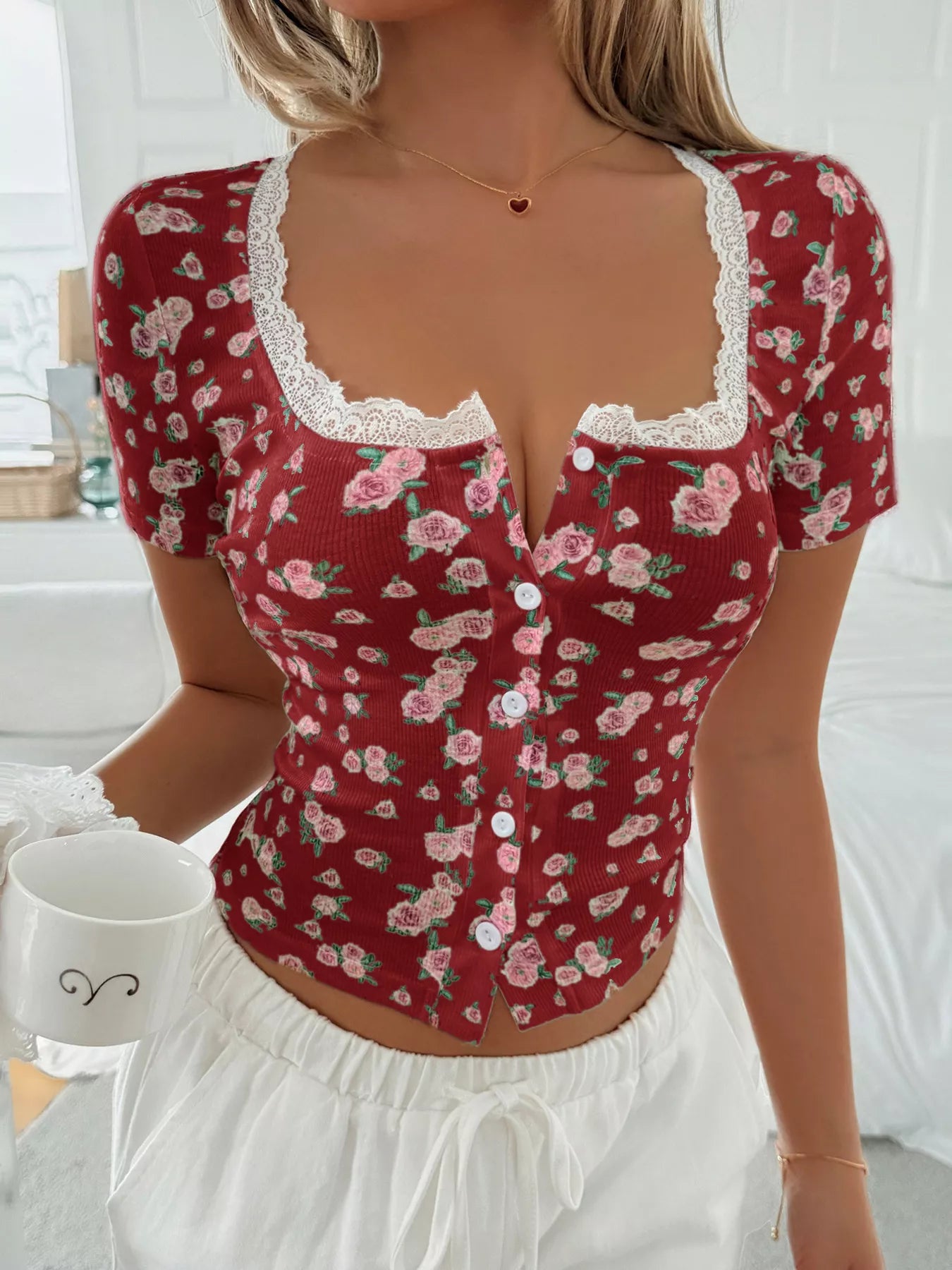 Woman wearing a red floral top with lace details in a bright room.
