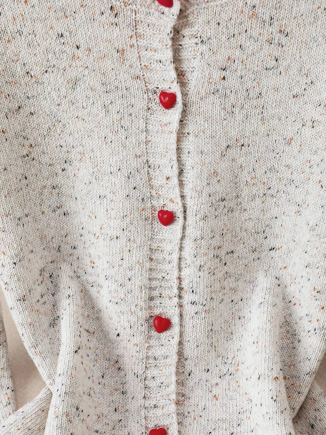 Close-up of a textured beige cardigan with red buttons.
