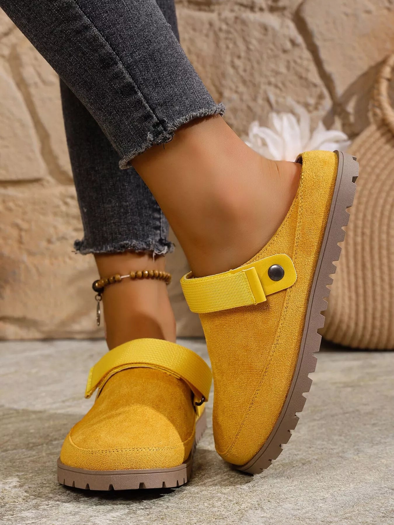 Yellow suede shoes with strap details worn by a person on a stone floor.