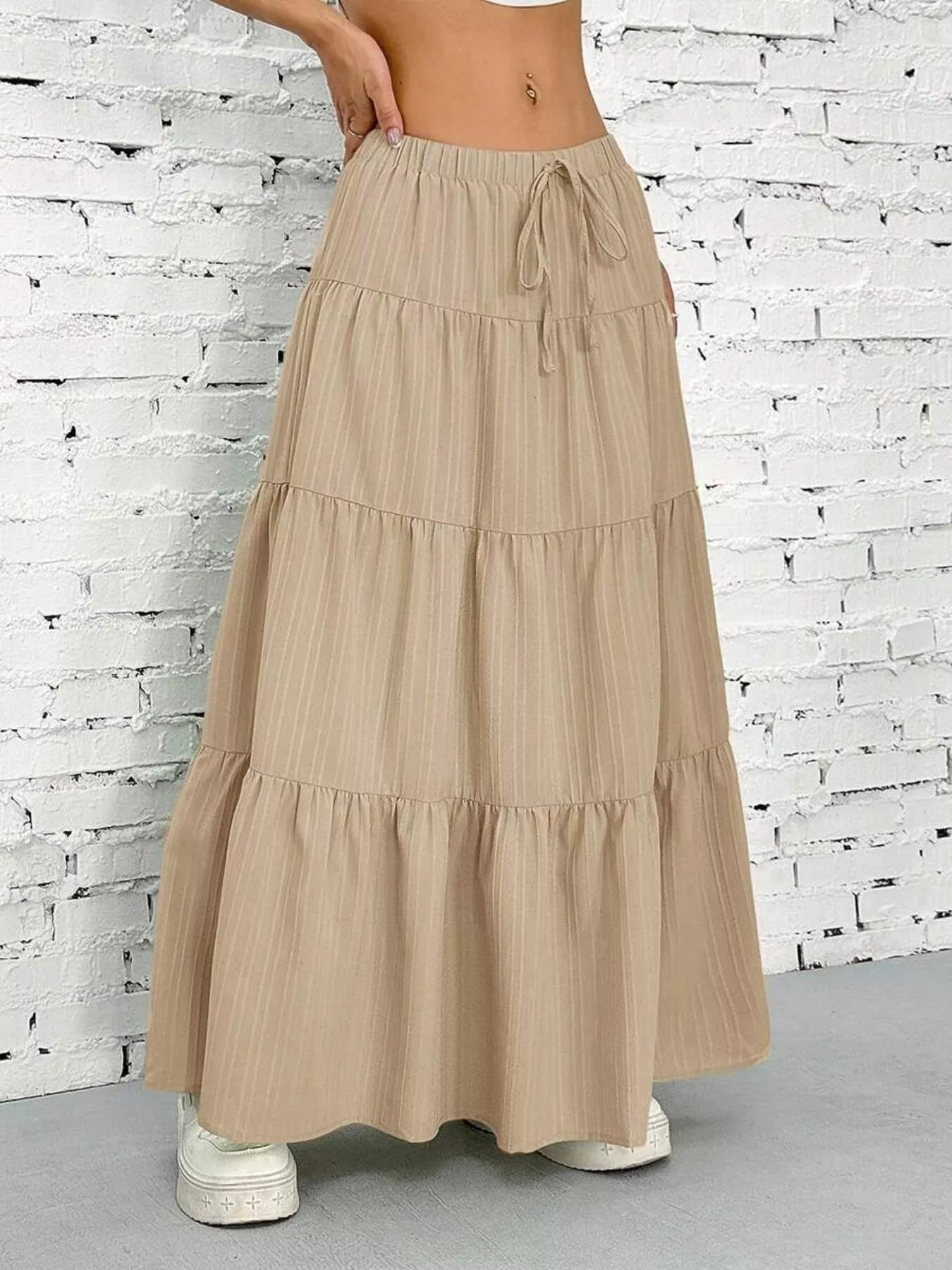 Beige tiered skirt worn by a person against a white brick wall.