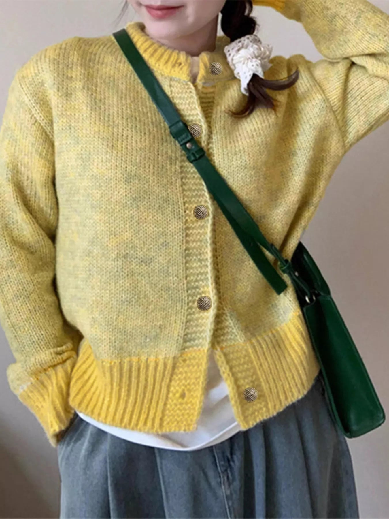 Person wearing a yellow knitted cardigan with a green bag over their shoulder.