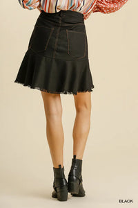 Black denim skirt worn with a colorful top and black boots on a beige background