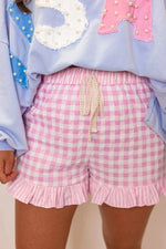 Person wearing a light blue sweater with decorative elements and pink checkered shorts.