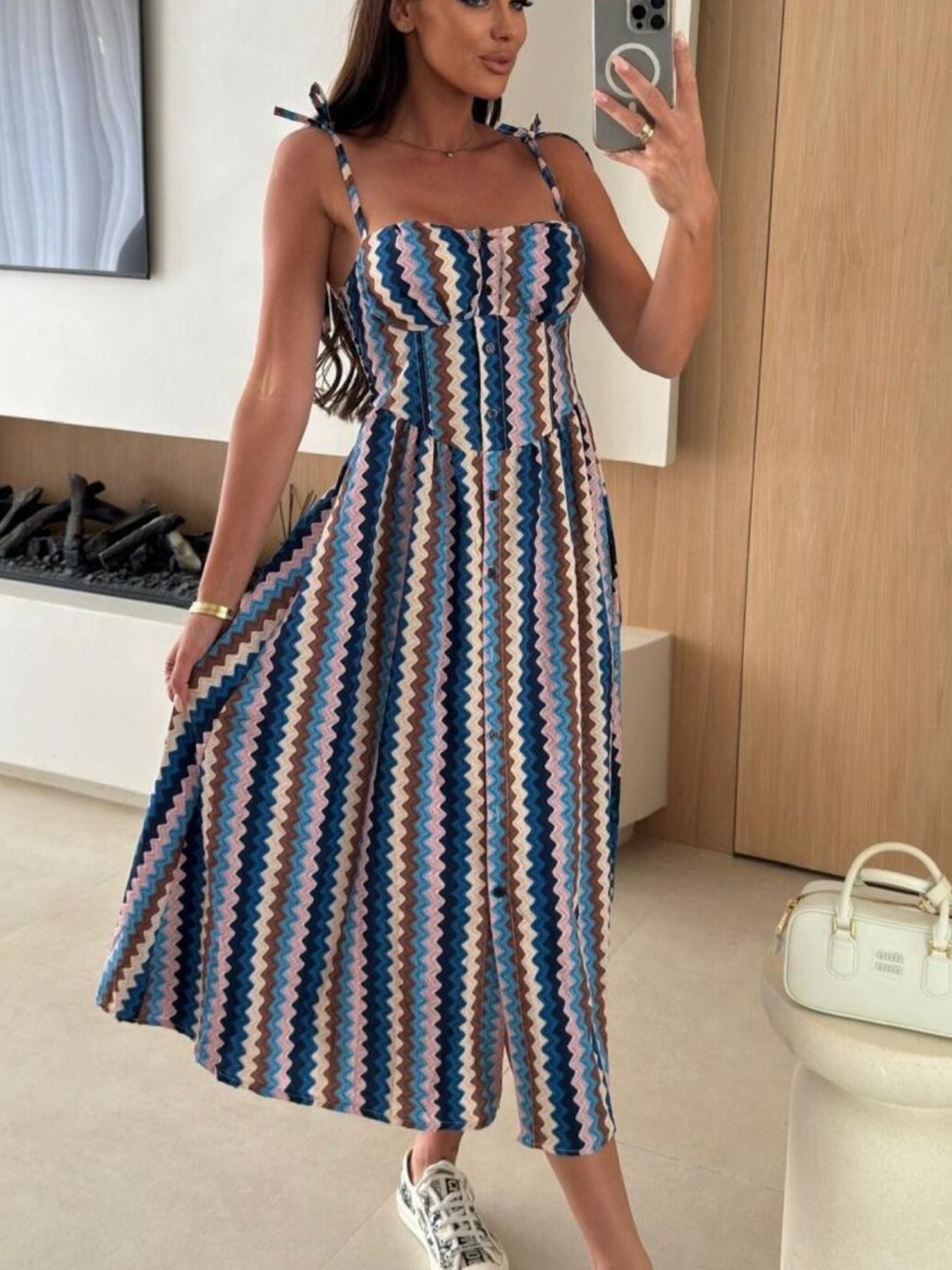 Woman taking a mirror selfie wearing a colorful striped dress in a room.