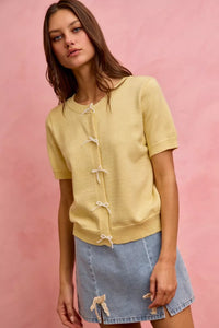 Woman wearing a yellow cardigan with white buttons against a pink background