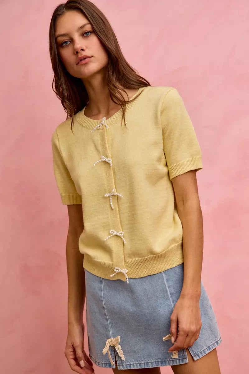 Woman wearing a yellow cardigan with white buttons against a pink background