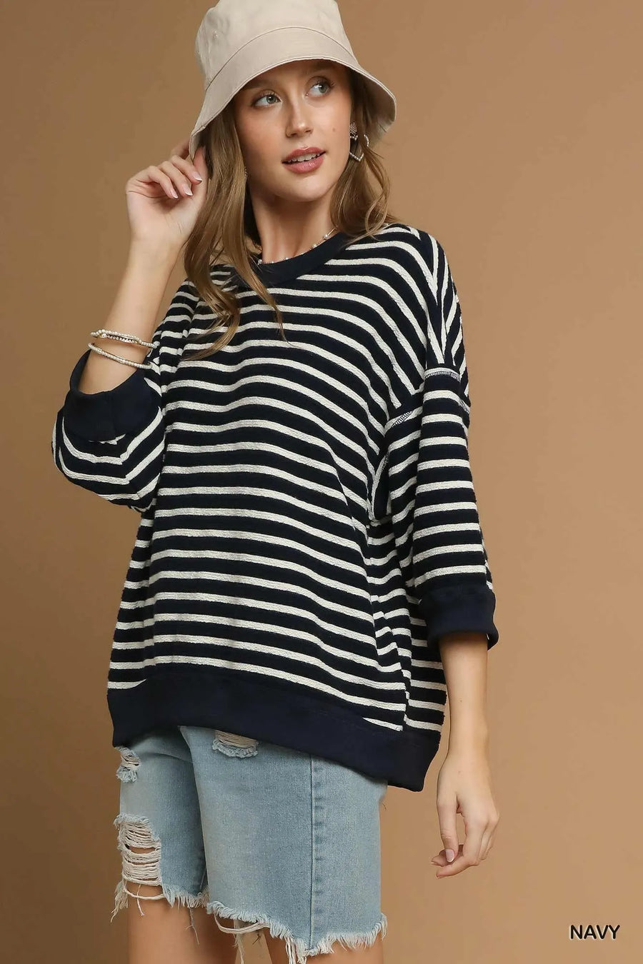 Woman wearing a black and white striped sweater with rolled-up sleeves and denim shorts on a brown background.