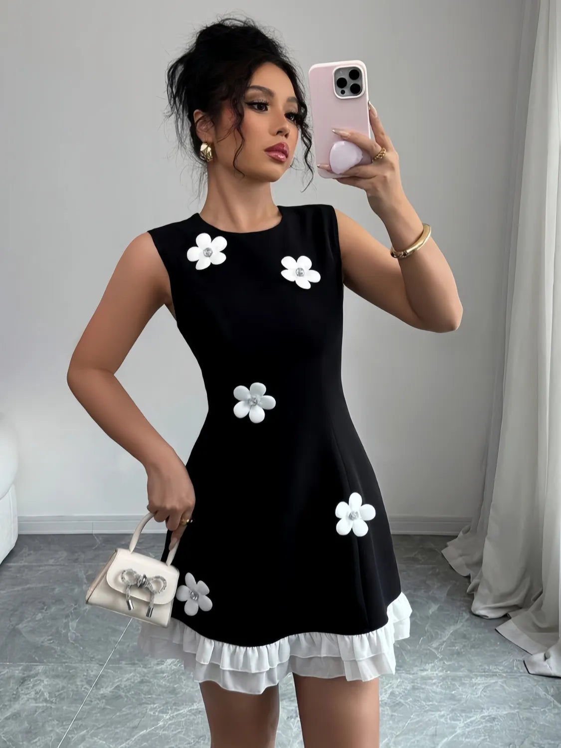 Woman taking a mirror selfie wearing a black dress with white floral patterns and holding a matching handbag.