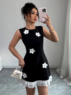 Woman taking a mirror selfie wearing a black dress with white floral patterns and holding a matching handbag.