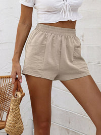 Person wearing beige shorts and a white top against a light-colored wall.