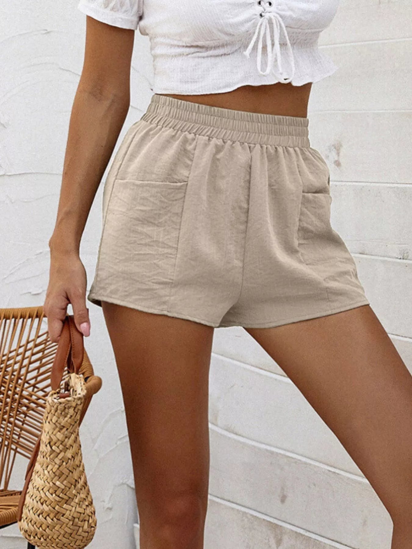 Person wearing beige shorts and a white top against a light-colored wall.