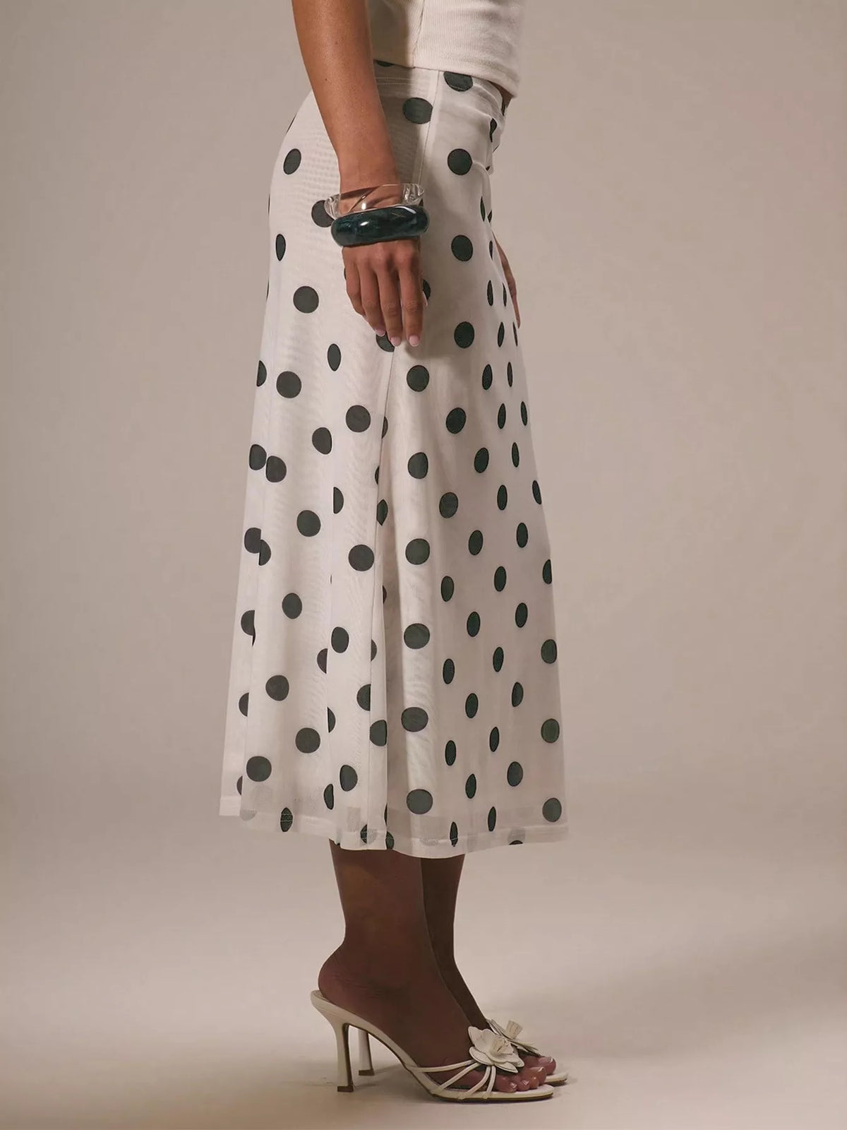 Person wearing a white skirt with black polka dots on a plain background
