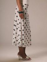 Person wearing a white skirt with black polka dots on a plain background