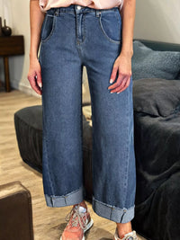 Person wearing blue jeans standing in a room with a couch and wooden floor.