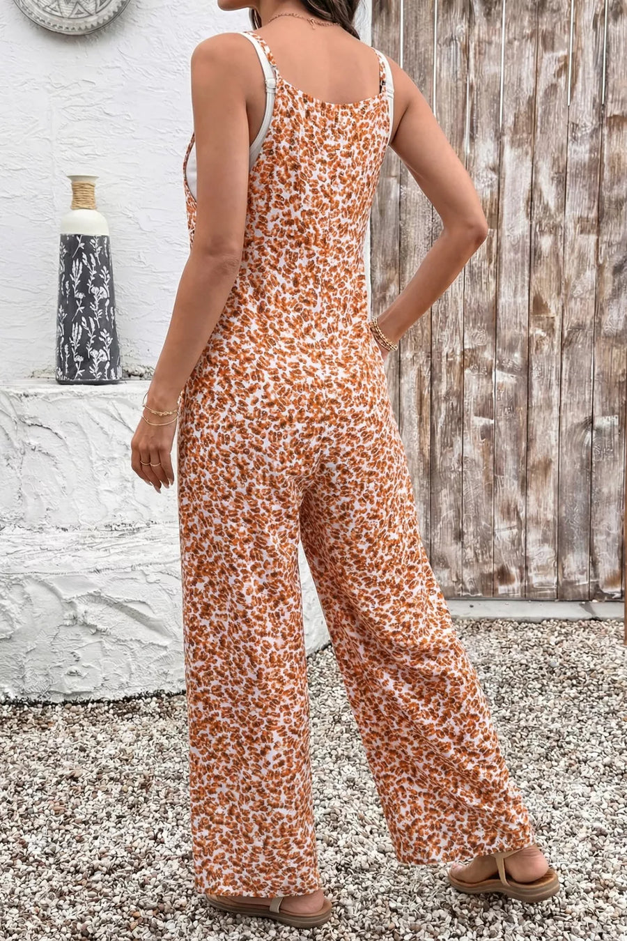Person wearing a floral jumpsuit standing against a rustic wooden wall.