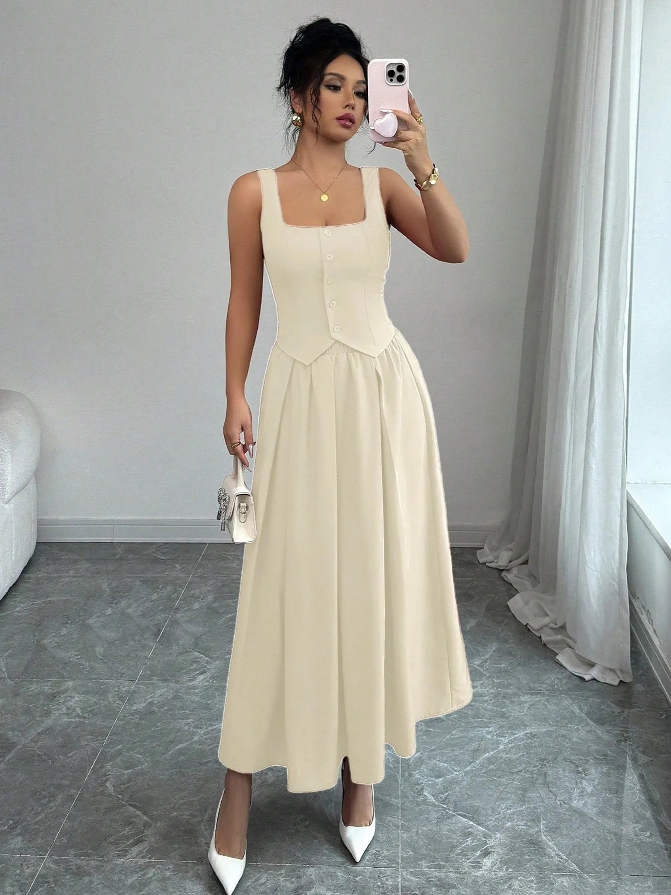 Woman taking a mirror selfie wearing a beige sleeveless dress in a room with white walls and gray floor.
