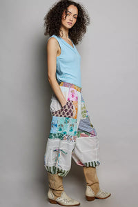 Woman wearing a light blue sleeveless top and colorful patchwork pants against a gray background