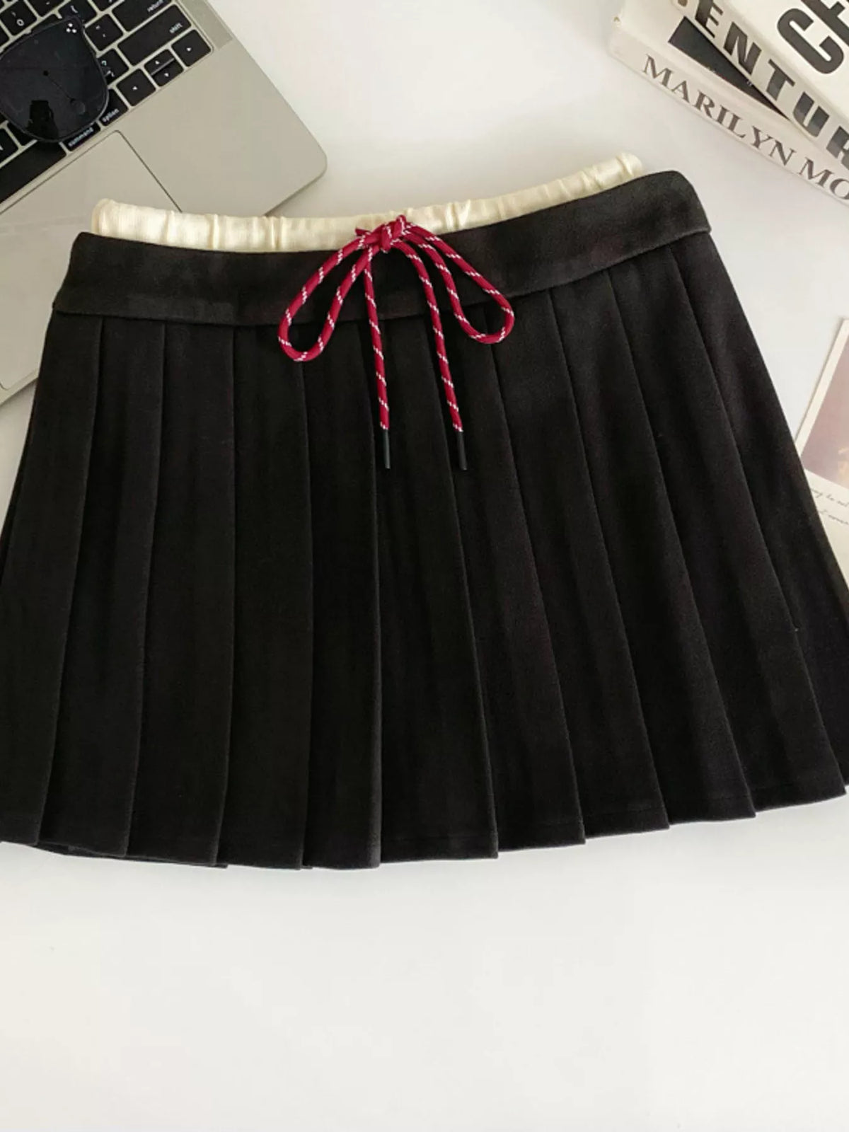 Black pleated skirt with a red drawstring on a white surface.