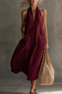 Woman wearing a burgundy dress holding a beige bag against a neutral background