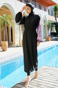 Woman in a black outfit standing by a pool with a building and plants in the background