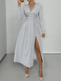 Woman wearing a gray long-sleeve dress with a high slit on a plain background