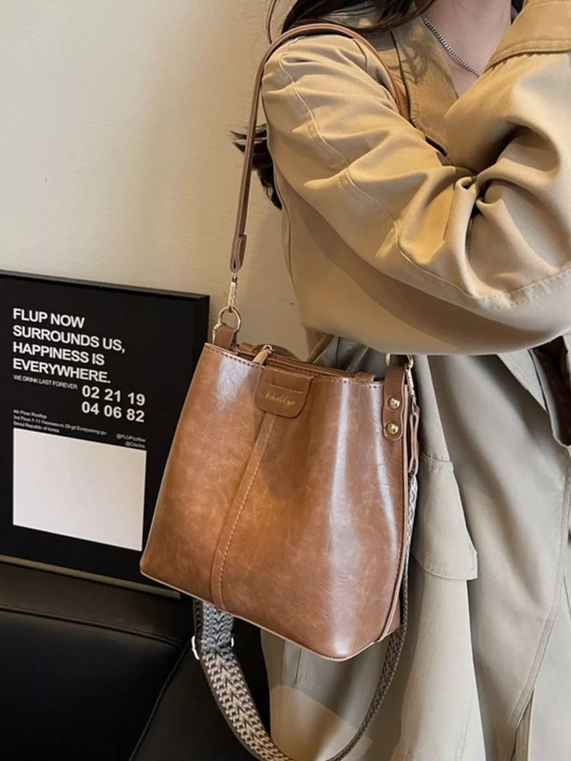 Person wearing a beige coat holding a brown leather handbag indoors.