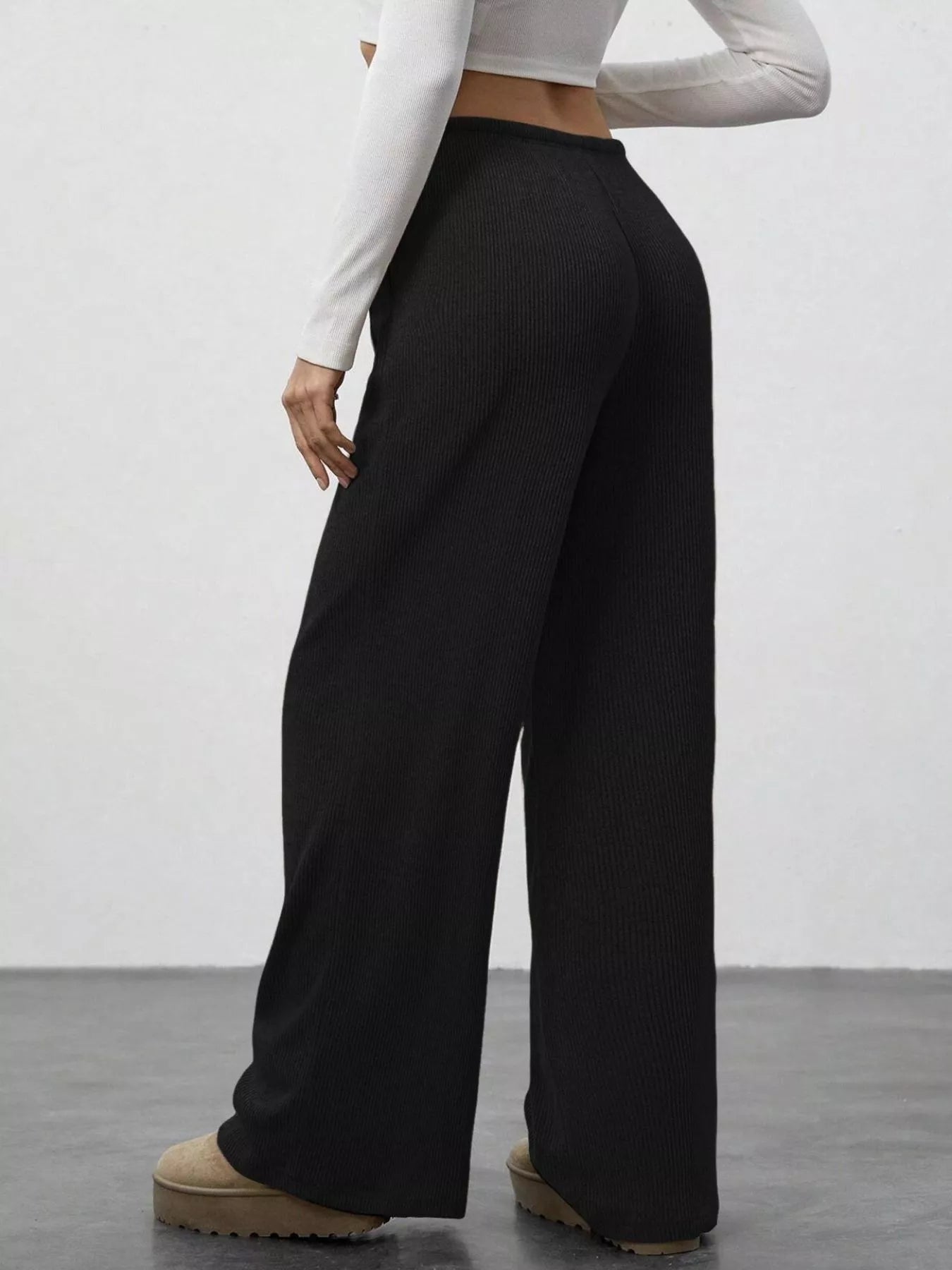 Person wearing black wide-leg pants and a white long-sleeve top on a plain background