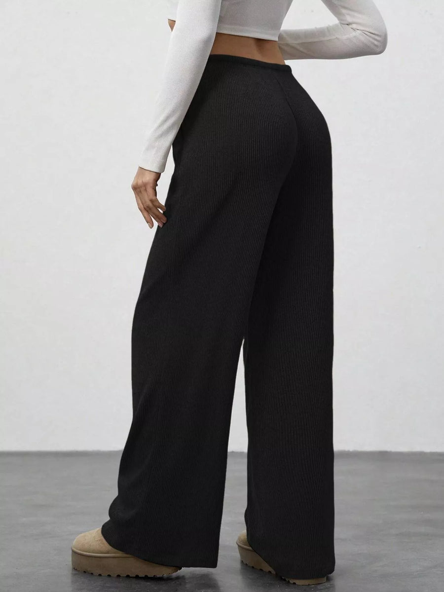 Person wearing black wide-leg pants and a white long-sleeve top on a plain background
