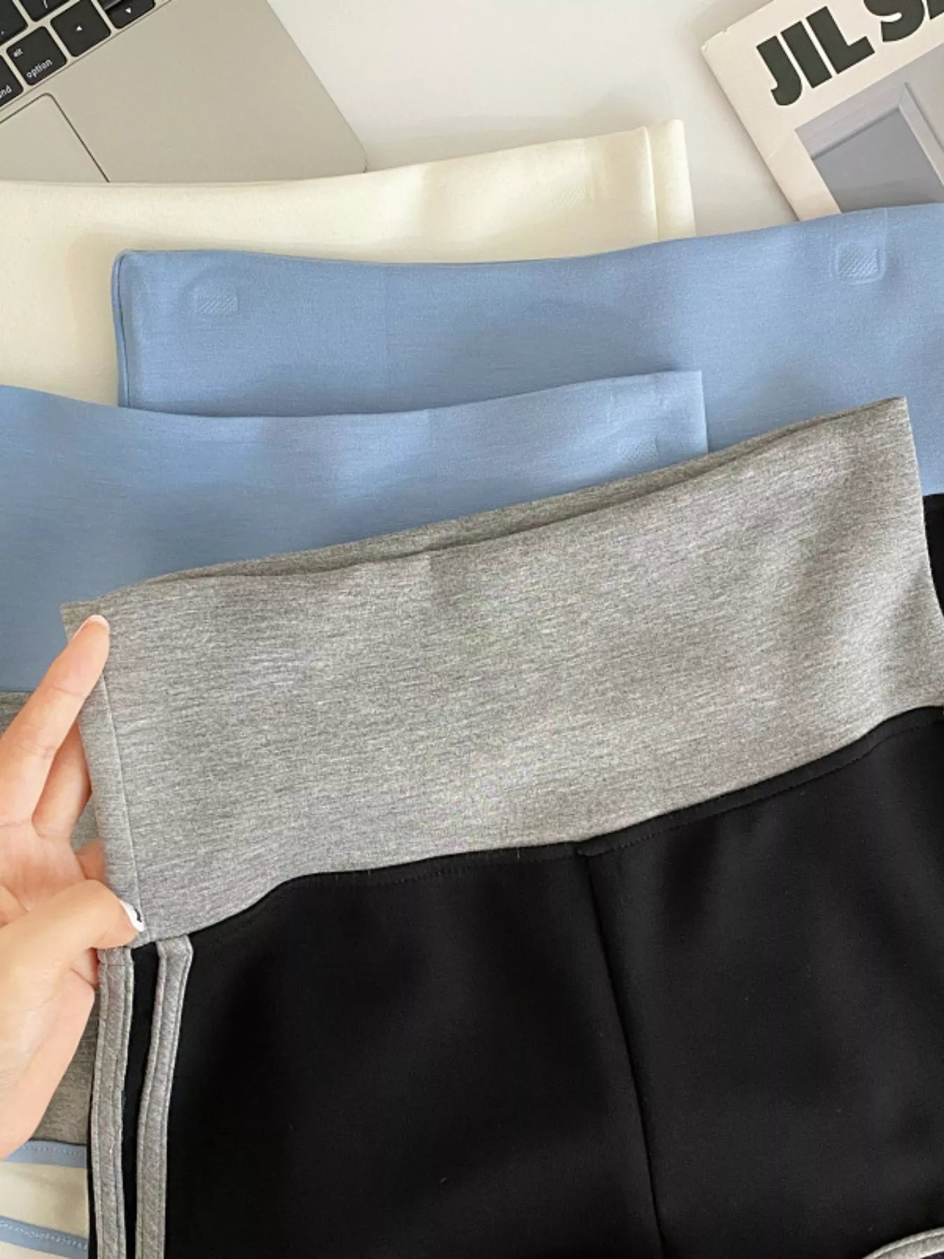 Gray and black fabric swatches held by a hand with a laptop and newspaper in the background.