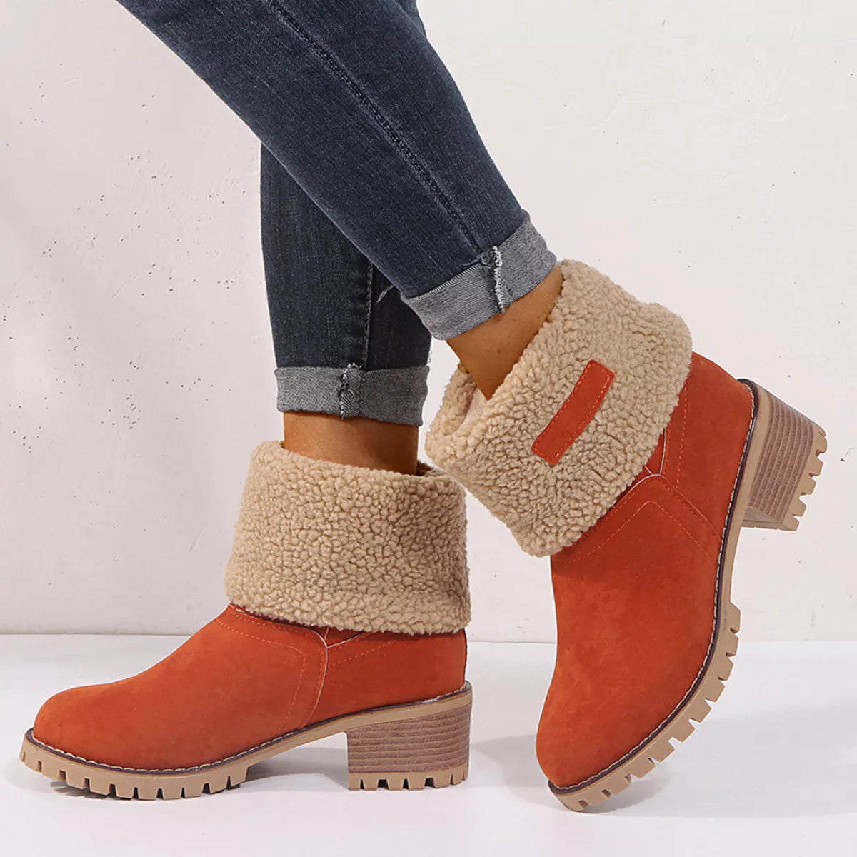Orange suede boots with beige shearling cuffs worn with blue jeans on a white background