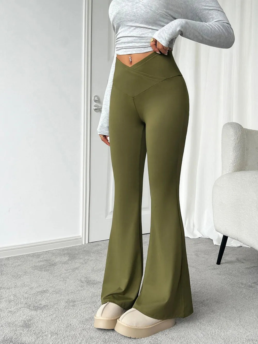 Person wearing olive green flared pants and a gray top in a minimalistic room.