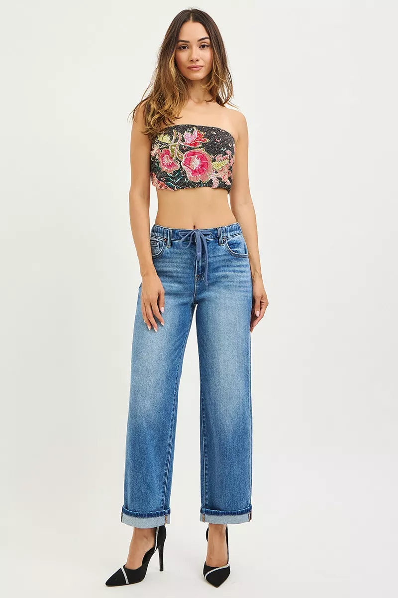 Woman wearing a floral bandeau top and blue jeans on a white background