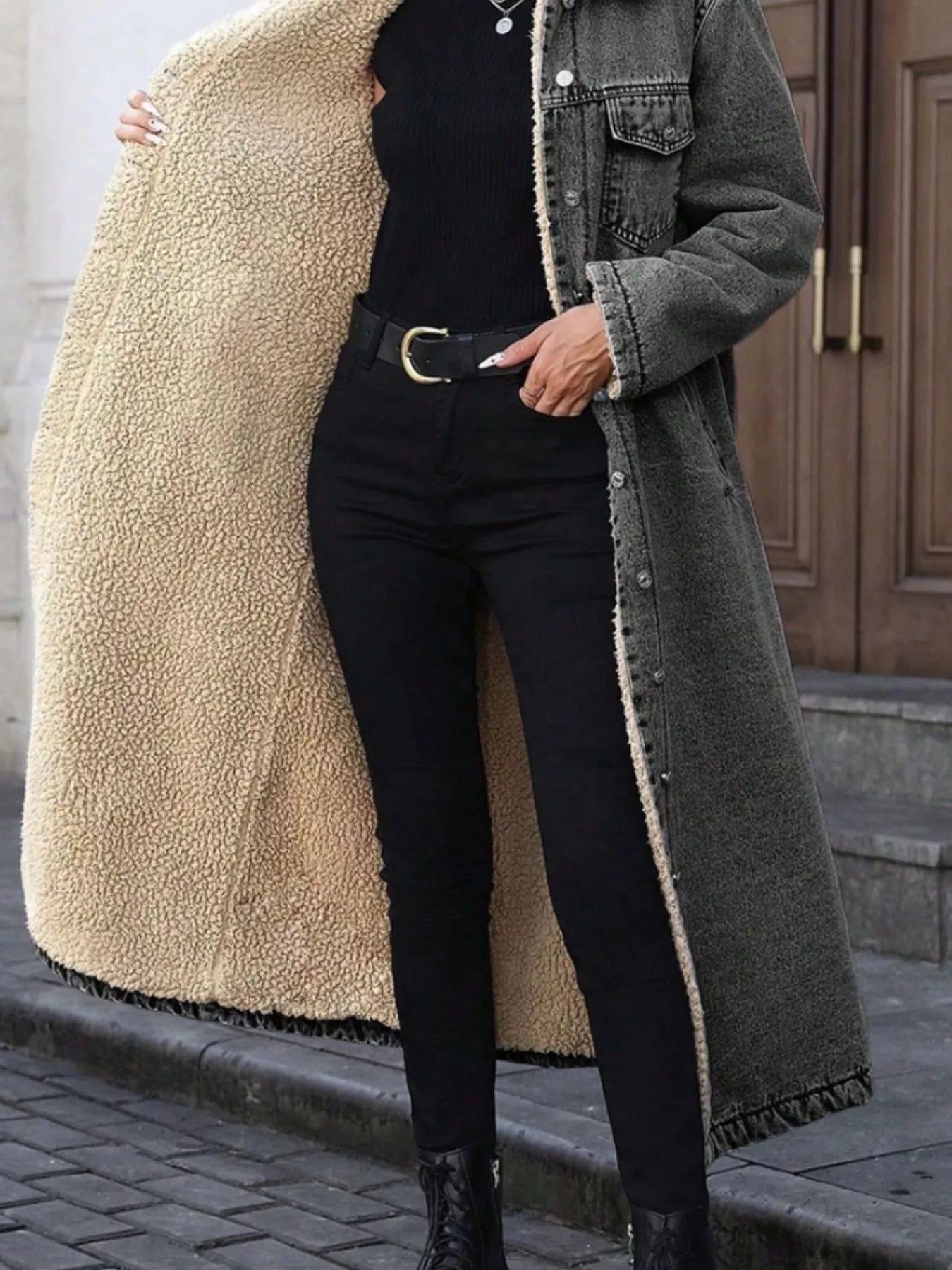 Person wearing a long coat with a beige sherpa lining, black pants, and black boots on a street.
