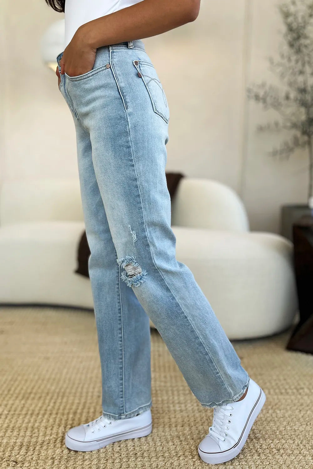 Person wearing light blue jeans and white sneakers in a room with beige walls and carpet.