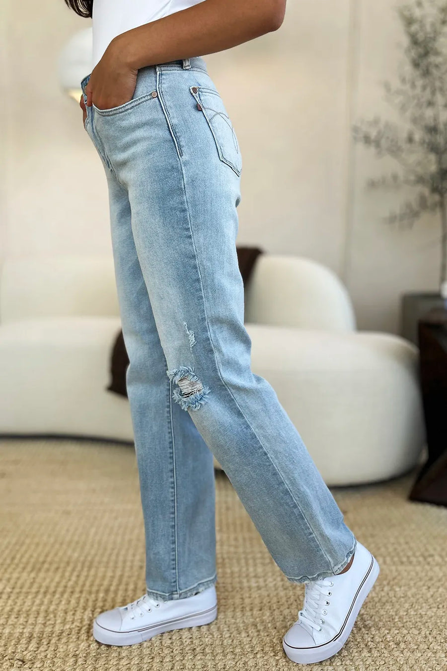 Person wearing light blue jeans and white sneakers in a room with beige walls and carpet.