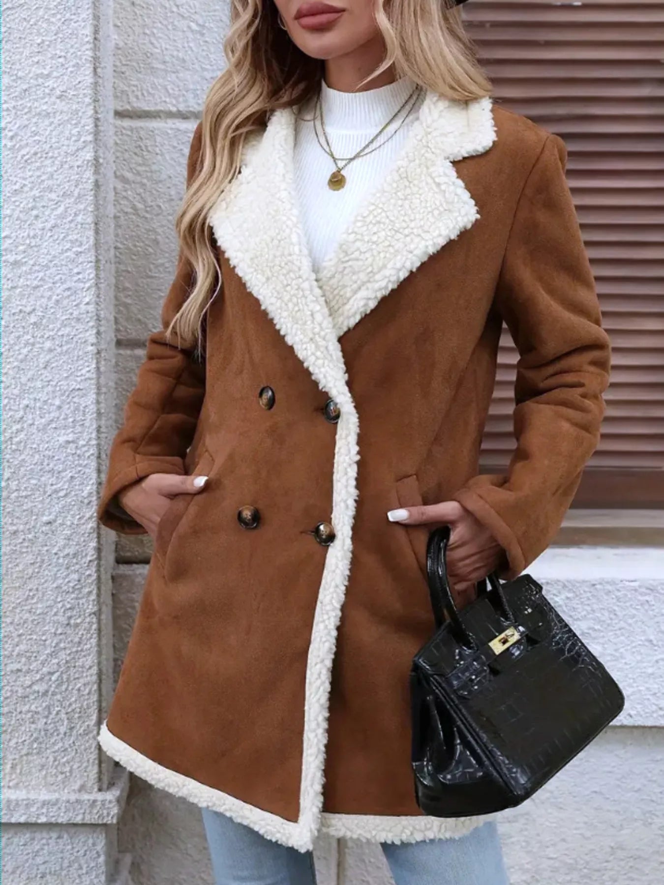 Woman wearing a brown coat with white fur lining, holding a black handbag.