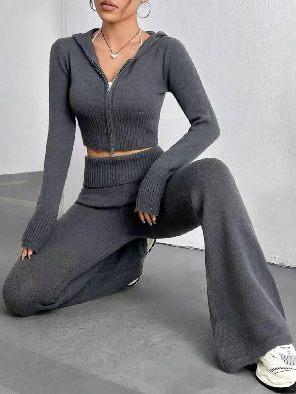 Person wearing a gray zip-up hoodie and matching pants sitting on a gray floor.