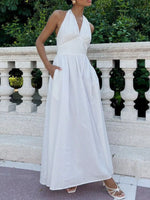 Woman in a white halter neck dress standing against a decorative stone wall.