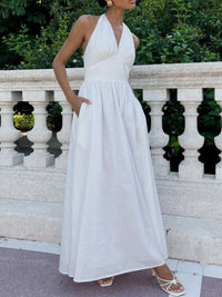 Woman in a white halter neck dress standing against a decorative stone wall.